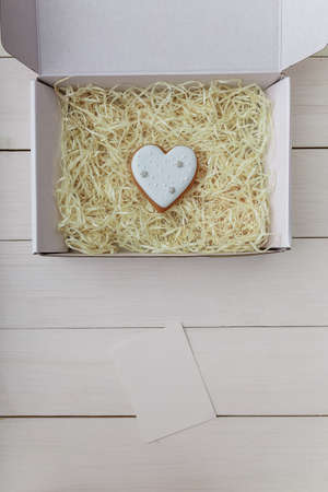 Present box and gingerbread cookie. Heart shape. Sweets on white wooden table background. 14 February Valentine's day concept, mock up. Place for text. Vertical shot.の写真素材