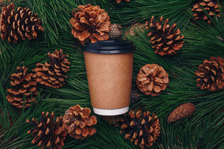 Green pine tree branches, cones background, paper cup of coffee mock up, top view. Merry Christmas beverage, hot drink for winter walk, social distancing, self-careの写真素材