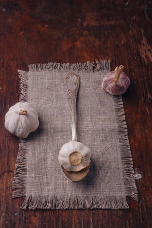 Some garlic bulbs on sackcloth, wooden table. Spicy vegetable, piquant flavoring, organic food, healthy eating, cooking ingredient. Vertical shotの写真素材