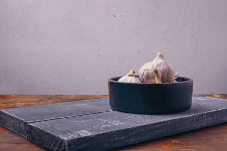 Some garlic bulbs in black pot, boards, kitchen background. Spicy aromatic plant, meal condiment, healthy eating, diet, nutrition conceptの写真素材