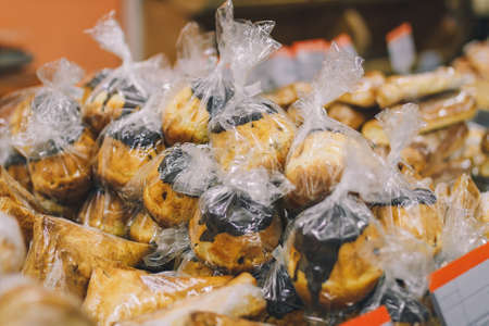 A lot of rum baba cakes with chocolate in polyethylene wrap on supermarket counter. Sweet tasty...