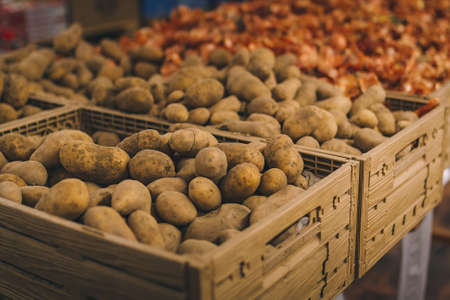 Wooden box of fresh potatoes in grocery department of shopping center, supermarket, mall. Unfocused onions on background.の写真素材