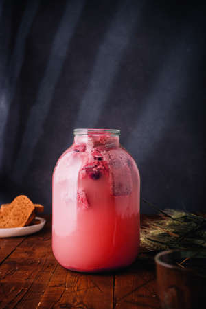 Jar of homemade bread and hibiscus kvass, wheat ears, slices of rye bread on wooden background....