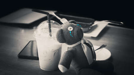 Teddy Bear sitting sadly on a wooden desk and Ice tea.の写真素材