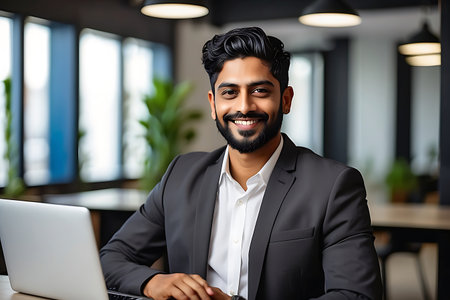 smiling indian businessman working on laptop at office desk in officeの素材
