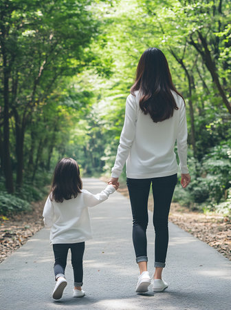 Back view of Asian mother and daughter walking together in the park.の素材