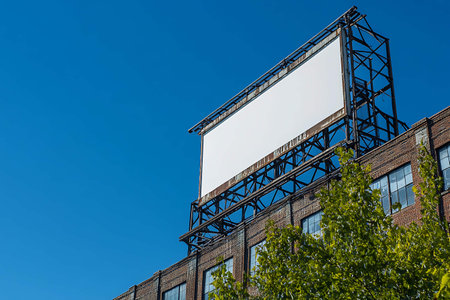 Large blank billboard on a brick building with a blue sky in the backgroundの写真素材