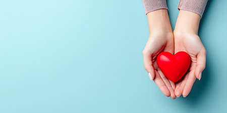 Female hands holding a red heart on a blue background with copy spaceの写真素材