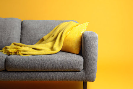 Comfortable sofa with yellow scarf on yellow background. Cozy home interiorの写真素材