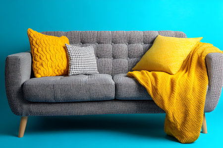 Comfortable sofa with yellow pillows and plaid on blue backgroundの素材