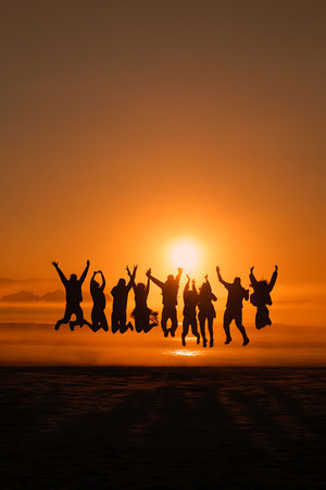 Silhouette of group of people jumping on the beach at sunsetの写真素材