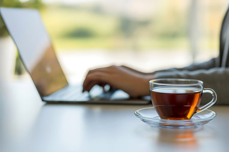 Closeup of businesswoman hands typing on laptop computer and drinking teaの写真素材