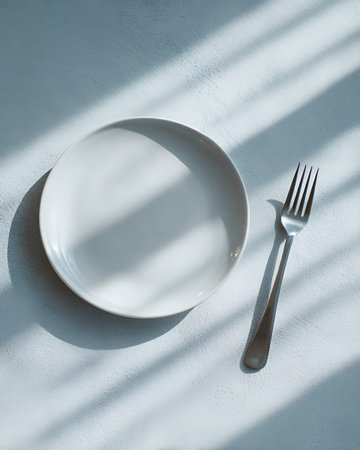 Empty white plate and fork on white background with shadow from window.の写真素材