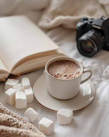 Cup of hot chocolate with marshmallows, book and camera on bed.の写真素材