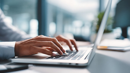 Close-up of male hands typing on laptop keyboard in modern officeの素材