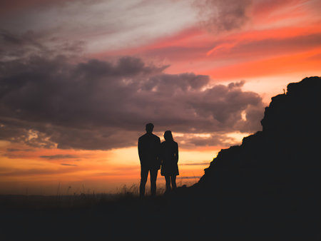 Silhouette of young couple on top of a mountain at sunsetの写真素材