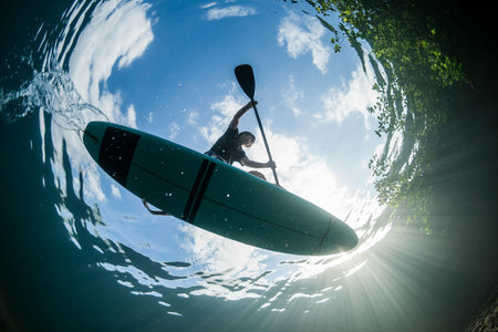 Man paddling a kayak in the ocean with sunbeamsの写真素材