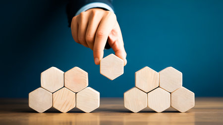 Businessman's hand placing wooden hexagons on the top of a wooden block.の写真素材