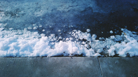 Snow piled on concrete ground, winter scene with frozen texture and icy surfaceの写真素材