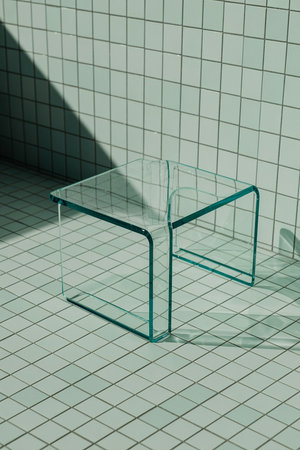 A sleek glass coffee table with a green tint stands on a tiled floor in a minimalist roomの写真素材