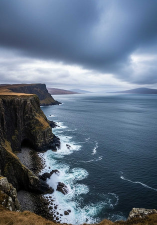 A dramatic coastal landscape with rugged cliffs and ocean waves under a stormy skyの写真素材