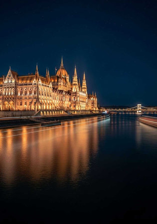 The Hungarian Parliament Building is illuminated at night beside a calm riverの写真素材
