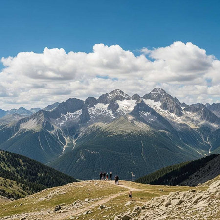 A group of people hiking on a mountain trail with a stunning view of snow-capped mountains in the backgroundの写真素材