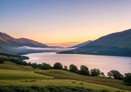 A serene landscape of a lake surrounded by mountains and trees at sunriseの写真素材