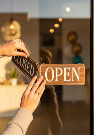 A person flips the open sign on a storefront door to indicate business hoursの写真素材