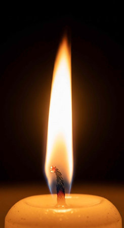 A lit candle with a bright flame burning steadily in the darknessの写真素材