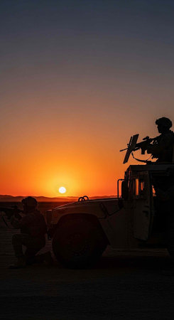 Soldiers in silhouette with a machine gun at sunset, desert landscape with a vehicleの写真素材