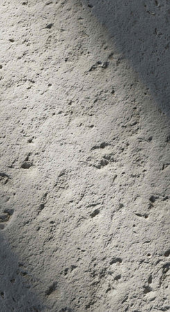 Gray concrete surface with small holes, rough texture, and varied lighting, showcasing detailed imperfectionsの写真素材