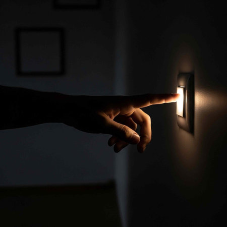 A hand reaching out to turn on a light switch in a dark room with a white wallの写真素材