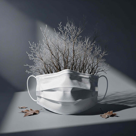 A white face mask with branches and leaves on a gray surface with a dark backgroundの写真素材