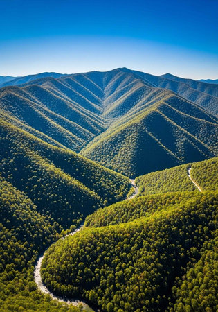Aerial view of a serene mountain landscape with a winding road and lush greenery under a clear blue skyの写真素材