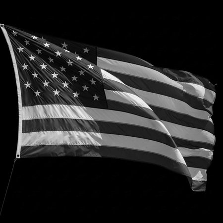 A black and white American flag waving in the wind against a dark backgroundの写真素材