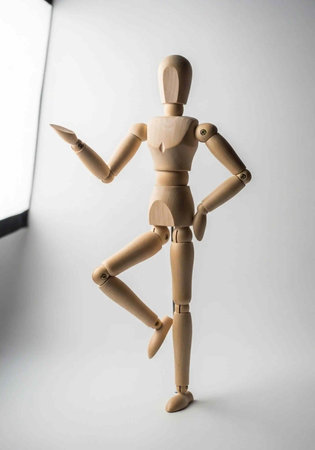 A wooden artist mannequin stands in a dynamic pose with one leg raised and arm extended against a studio lighting backgroundの写真素材