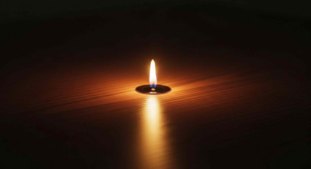 A small candle burns brightly in the darkness, casting a warm glow on the surrounding surface.の写真素材