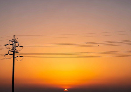 Electric power lines and tower stand against colorful sunset with orange, yellow, and purple hues in the skyの写真素材