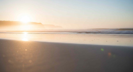 Peaceful beach scene at dawn with golden sunlight, gentle waves, and smooth wet sand reflecting the sun's raysの写真素材