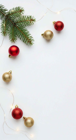 Festive arrangement of red and gold Christmas ornaments, pine branch, and fairy lights on a white surfaceの写真素材