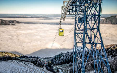 Cable-way and yellow cable car in Alps. View of Alps from above cloudsの写真素材
