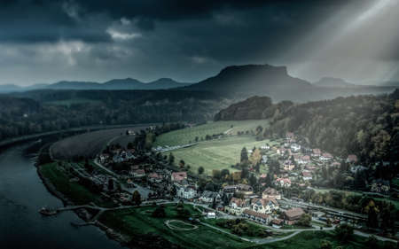Small city in Saxon Switzerland National Park on Elber river under sun rays breaking through the heavy clouds.の写真素材
