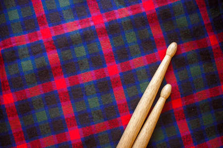 Two drum sticks of oak for rock and roll  lie on the fabric of a Scottish cage textile