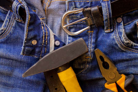 The hammer and pliers lie on blue working jeans trousers with a black leather beltの写真素材