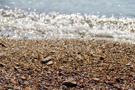 Small rocky beach with an incident wave of pebbles and foam near the shoreの写真素材