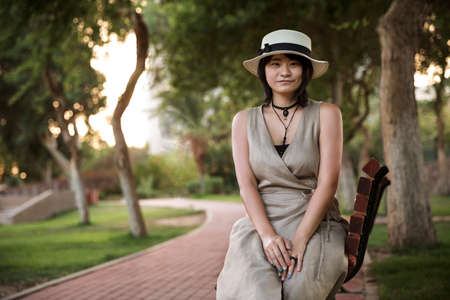 Beautiful young asian student girl sitting in the park on the bench in good weatherの写真素材
