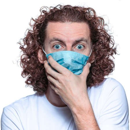 Man in medical mask looks in camera. Scared man in fear of coronavirus stands in protective medical mask against viruses and infections isolated studio. Coronavirus 2019-ncov covid-19 concept.の写真素材