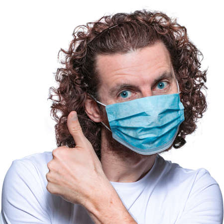 Man in medical mask looks in camera. Scared man in fear of coronavirus stands in protective medical mask against viruses and infections isolated studio. Coronavirus 2019-ncov covid-19 concept.の写真素材