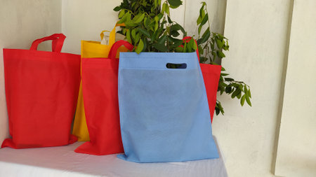 Assorted Color Non Woven Bags with green leaves isolated on white desk. ECO Friendly Shopping bags for mock-up. Copy space Concept for text. New Year and Christmas Gift Bags.の写真素材